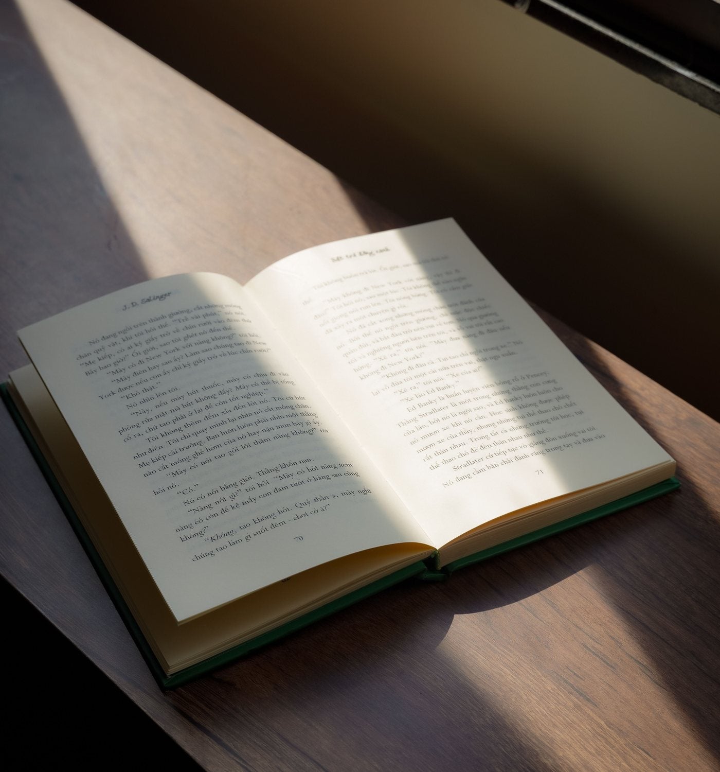 Open book on a sunlit wooden table, showing everyday room texture