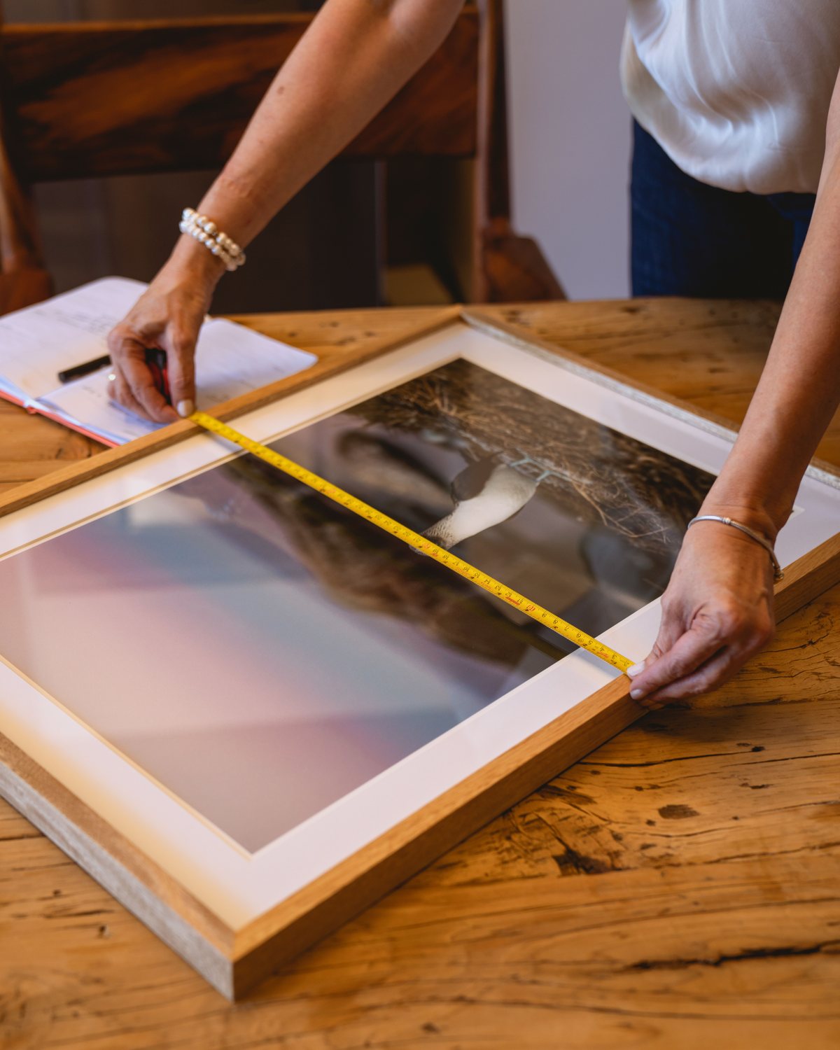 A framed artwork being measured on a wooden table before hanging